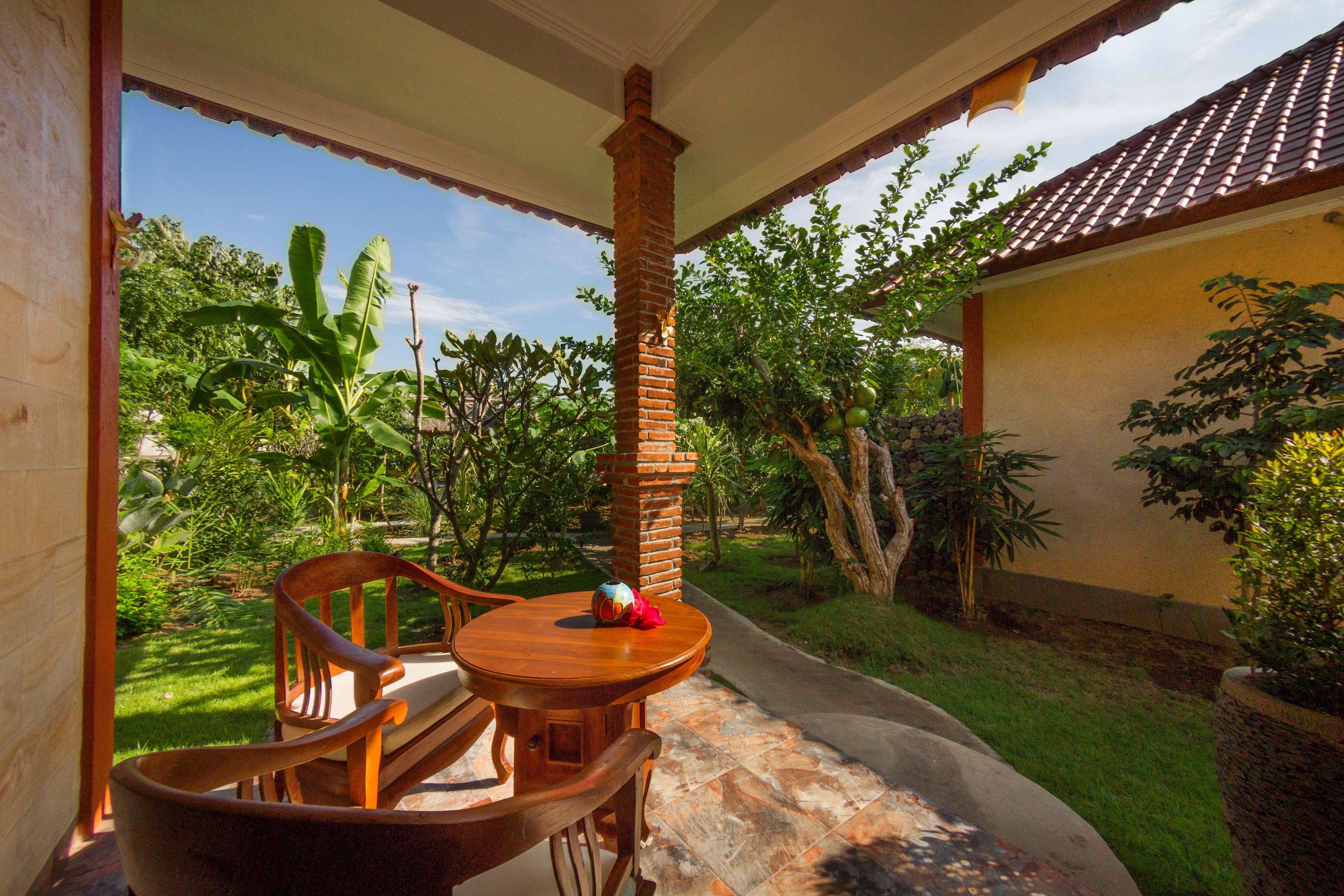 A covered outdoor seating area with a brick pillar, wooden chairs, and a small table.