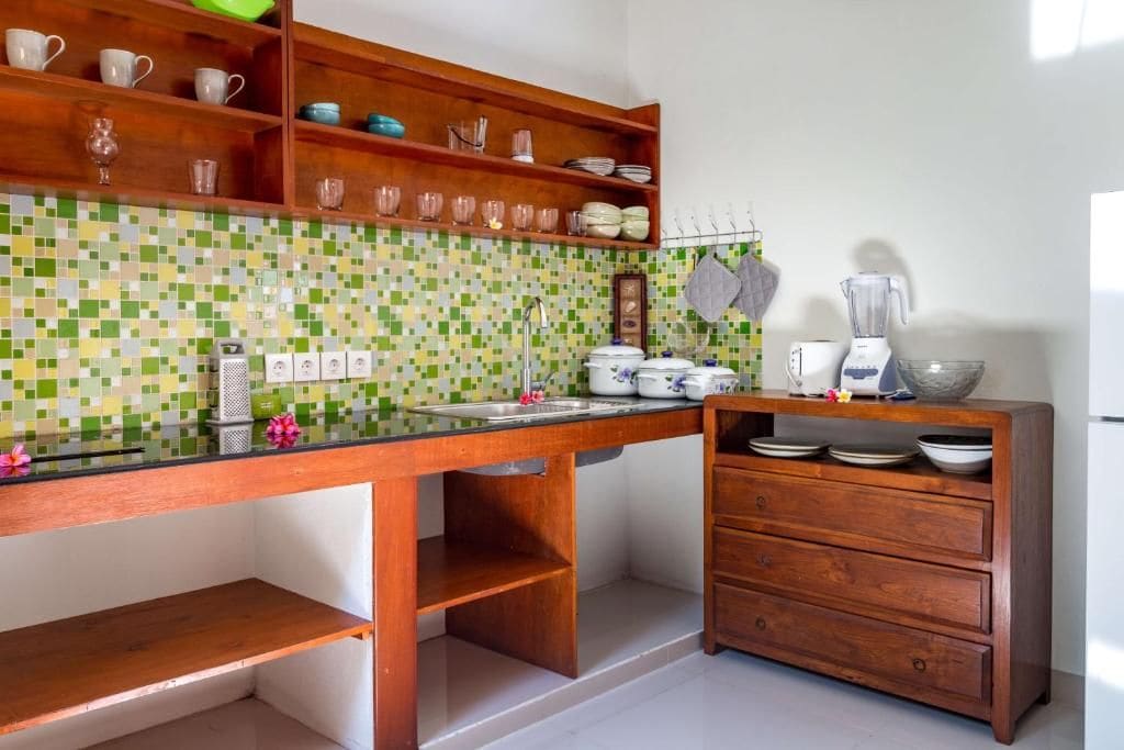 A kitchen with a tiled backsplash, wooden shelves, a countertop, and a built-in cabinet.
