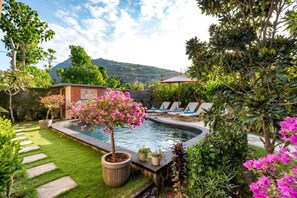 Une piscine avec un espace jardin, des chaises longues et une vue sur les montagnes en arrière-plan.