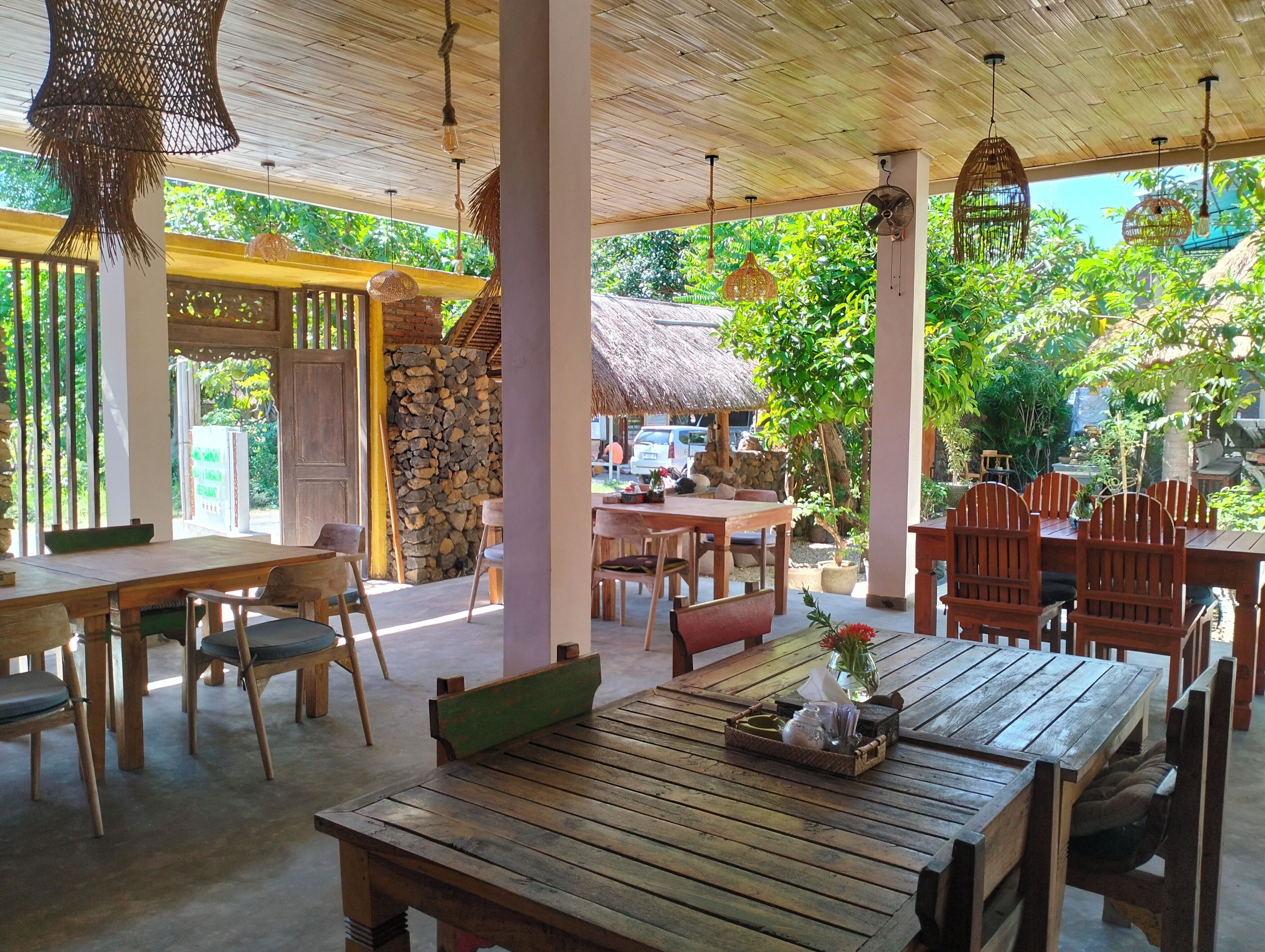 Un espace de restauration en plein air avec des tables et des chaises en bois, un mur en pierre et des lampes en osier suspendues.