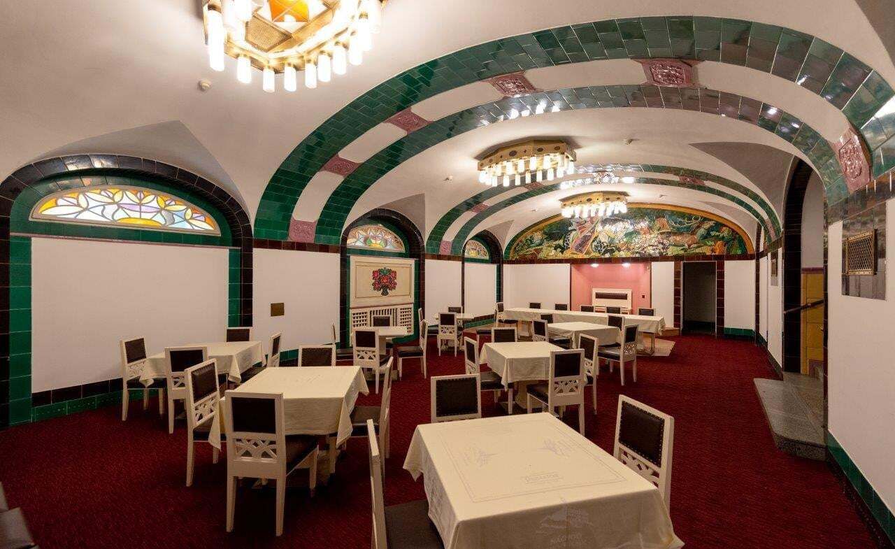 A dining area with tables and chairs, arched ceilings, and a red carpet.