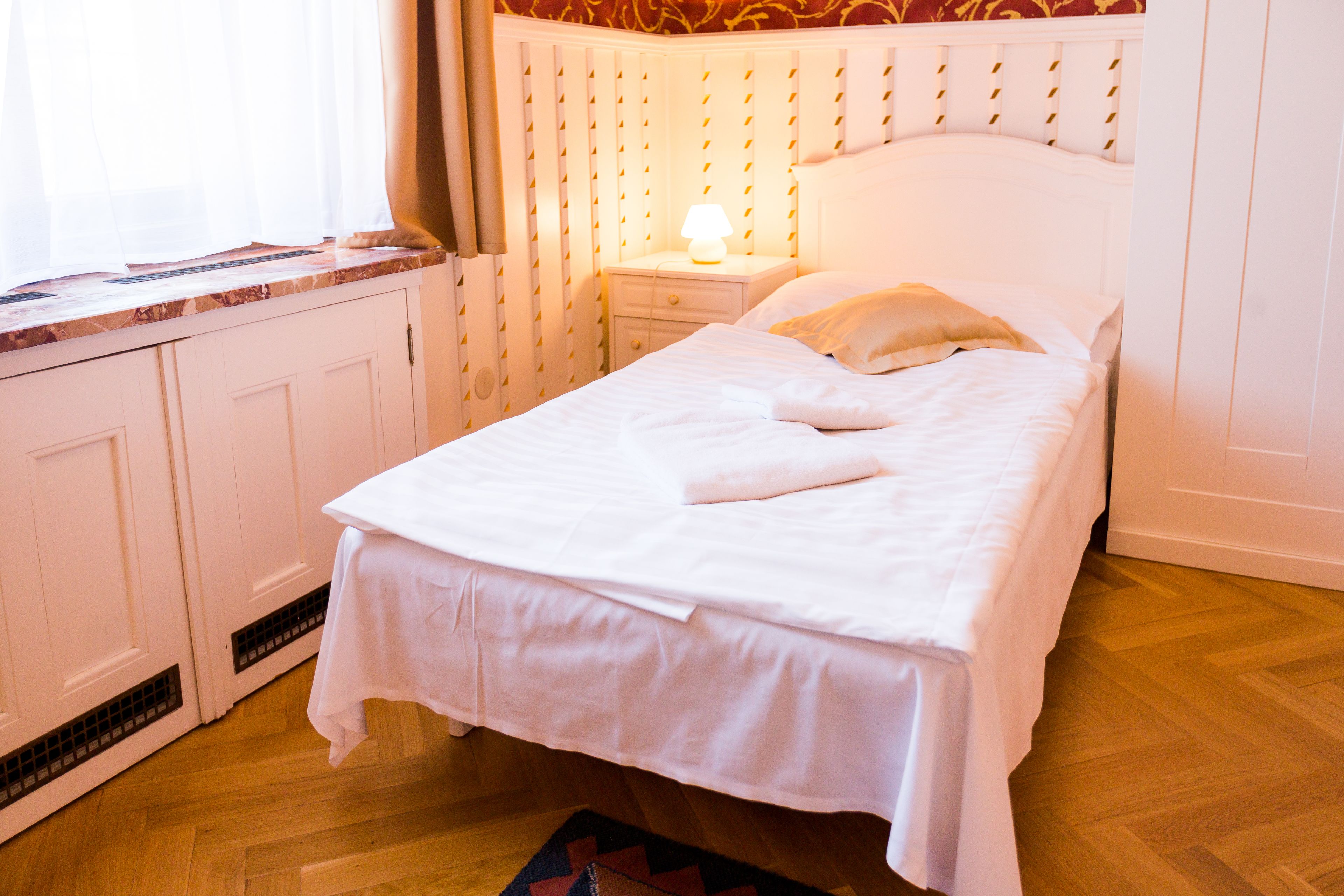 Un lit bien fait, recouvert d’une couvre-lit blanche et agrémenté d’oreillers, une table de chevet avec une lampe et une fenêtre avec des rideaux.