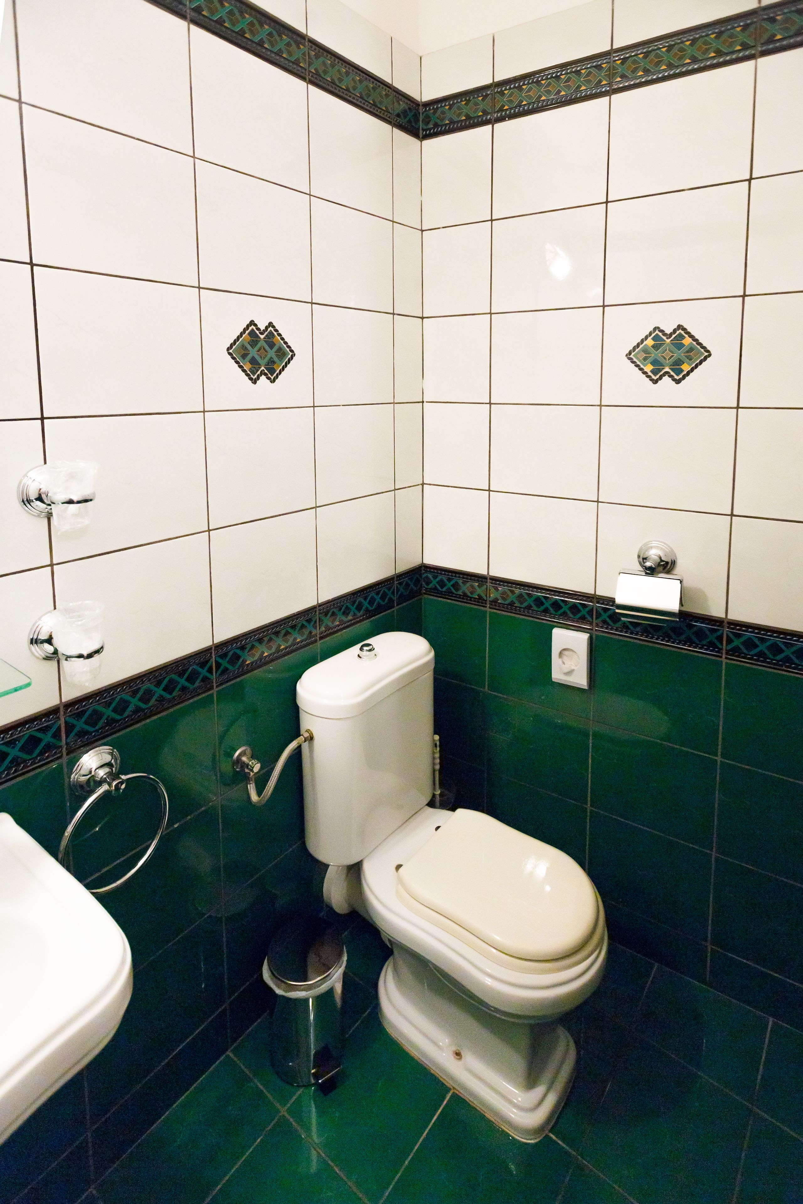 Une salle de bain avec des carreaux blancs, des carreaux verts, des toilettes, un bidet et une poubelle.