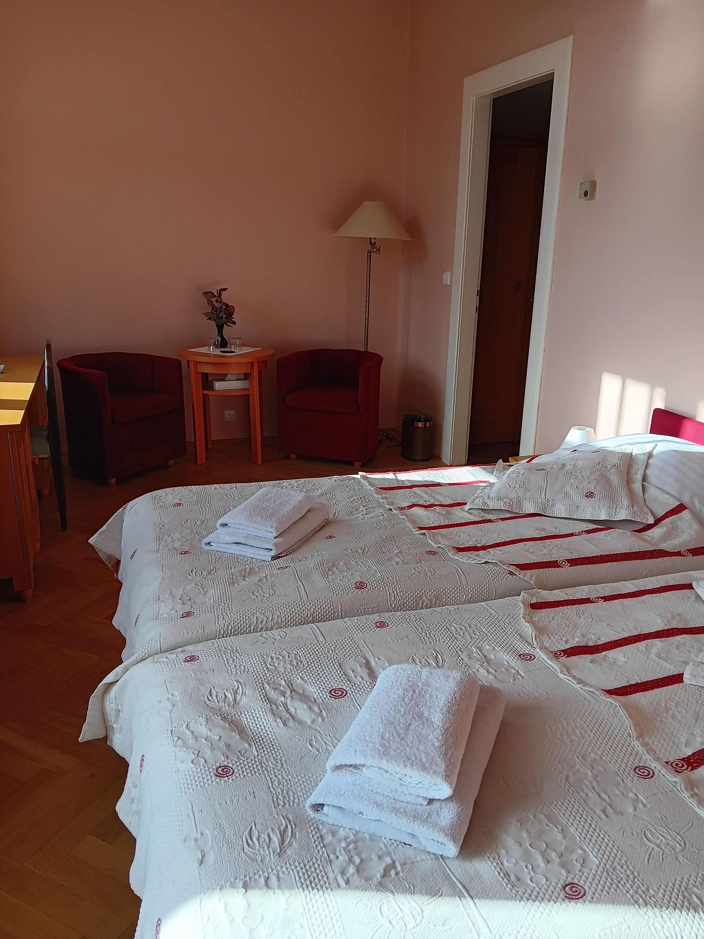 Een hotelkamer met twee bedden, een bureau, twee stoelen, een lamp en een deur.