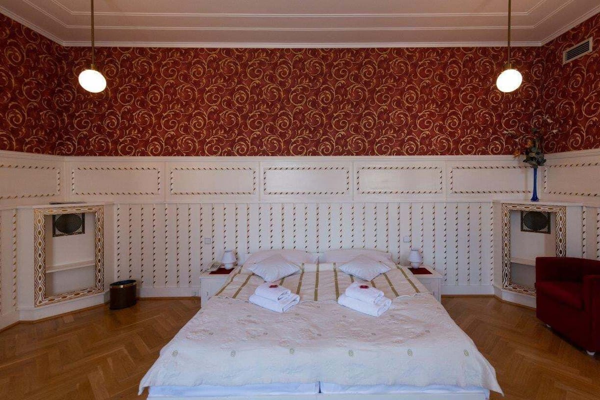 A hotel room with a large bed, a red armchair, and a decorative mirror.