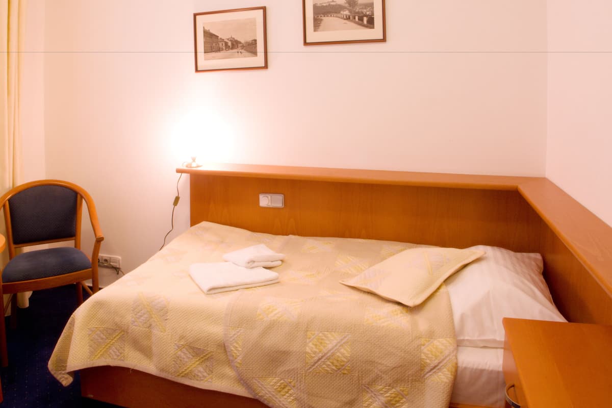 A hotel room with a bed, a chair, and two framed pictures on the wall.