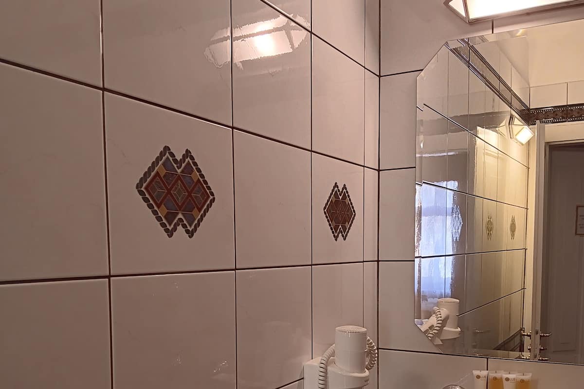 A bathroom with white tiles, a mirror, a sink, and a hairdryer.