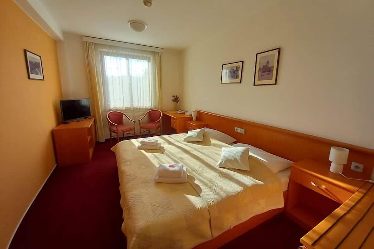 A hotel room with a large bed, a desk, a chair, a television, and two framed pictures on the wall.