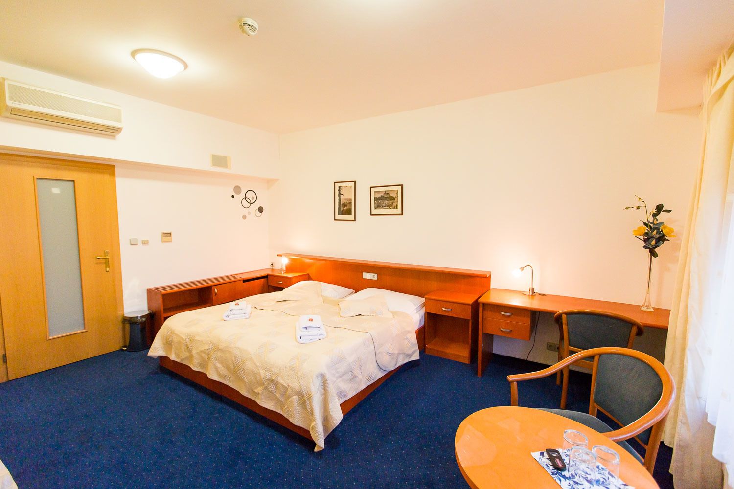 A hotel room with a bed, a desk, a chair, and a small table.
