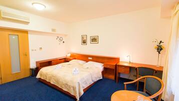A hotel room with a bed, a desk, a chair, and a small table.