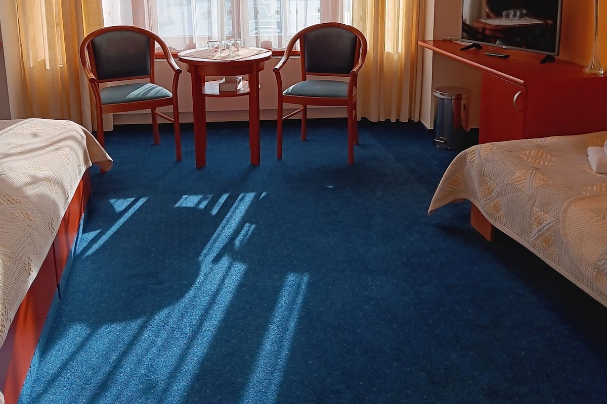 A hotel room with two beds, a round table with chairs, a TV, and a window with curtains.