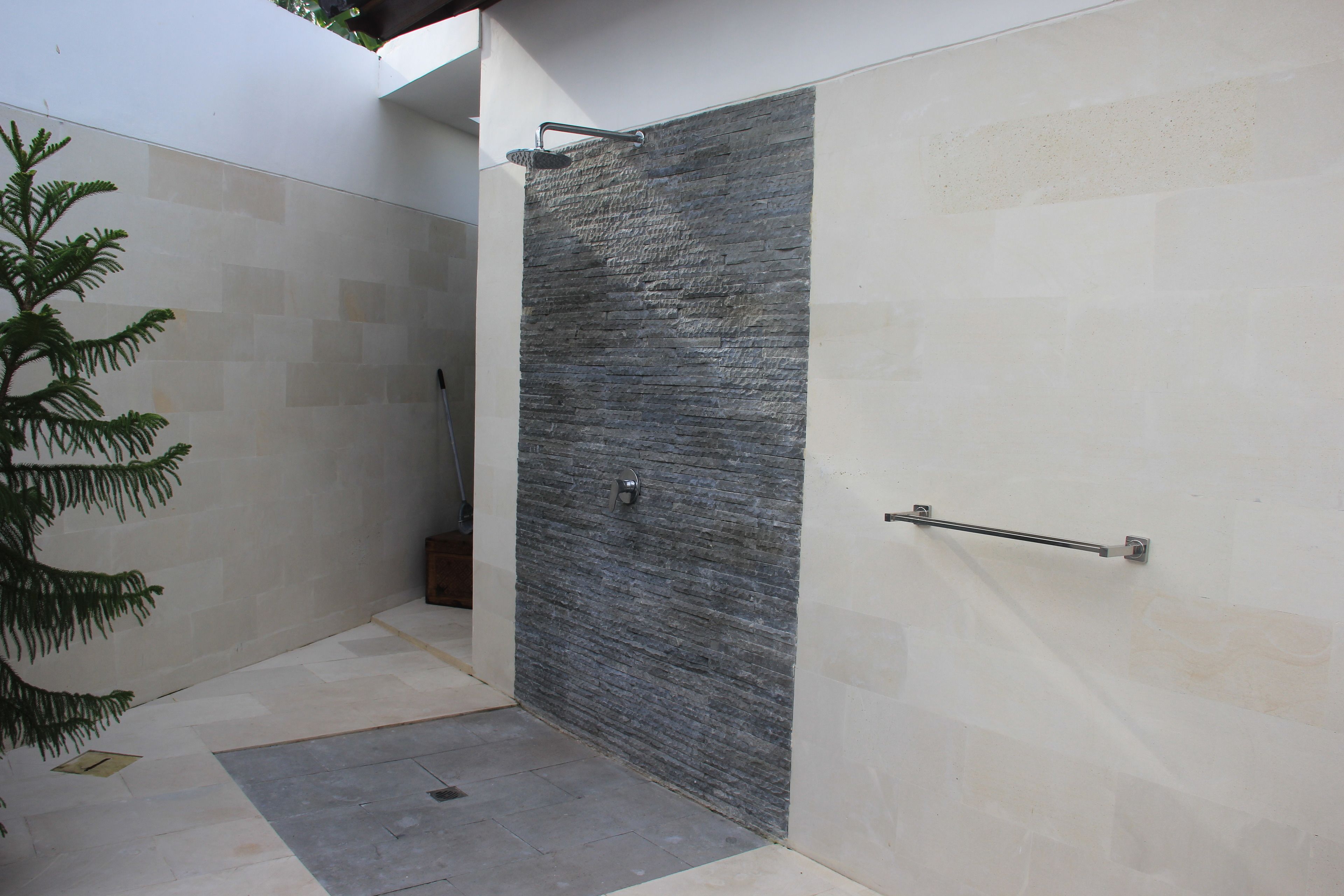 A modern bathroom with a stone wall, a shower area, and a potted plant.