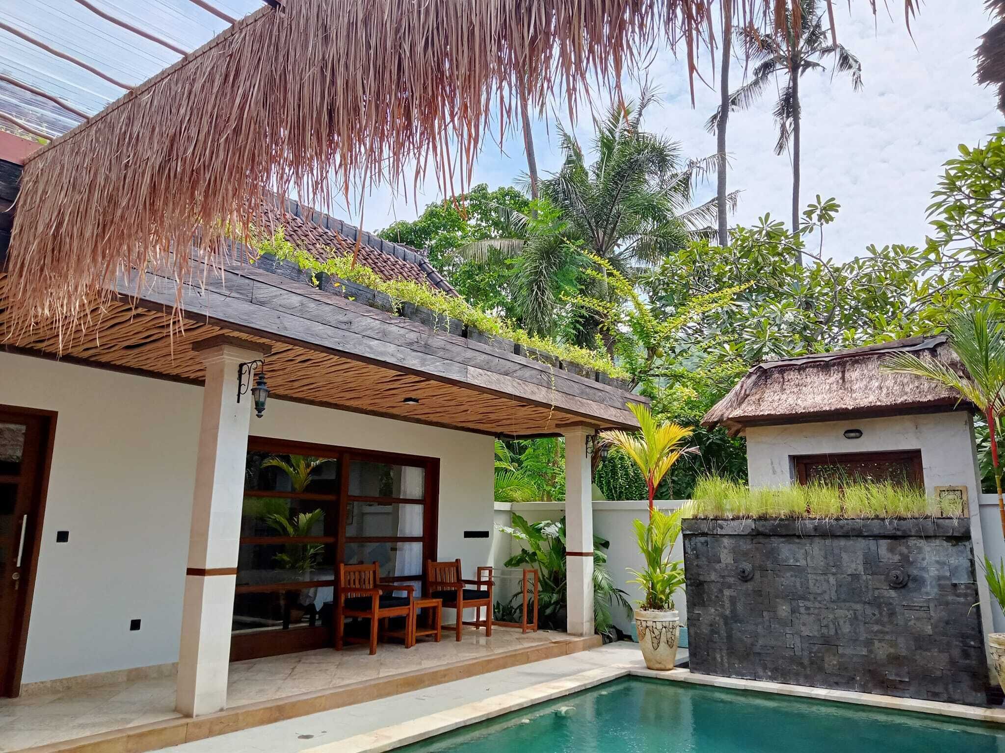 A poolside area with a covered seating area, a stone wall, and lush greenery.