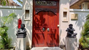 Une porte rouge ornée d’une partie supérieure décorative, flanquée de deux statues sur des piédestaux, et le chiffre « 23 » au-dessus de la porte.