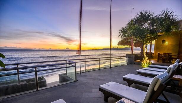 Une terrasse avec des fauteuils, une table et une vue sur la mer au coucher du soleil.