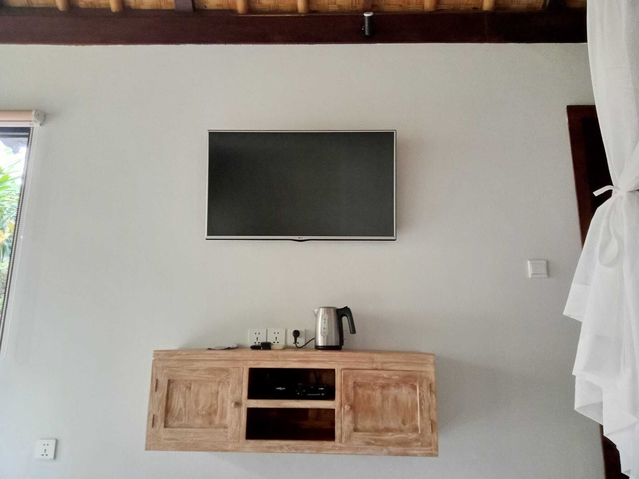 A room with a mounted flat-screen TV, a wooden cabinet with a coffee maker, and a power outlet.