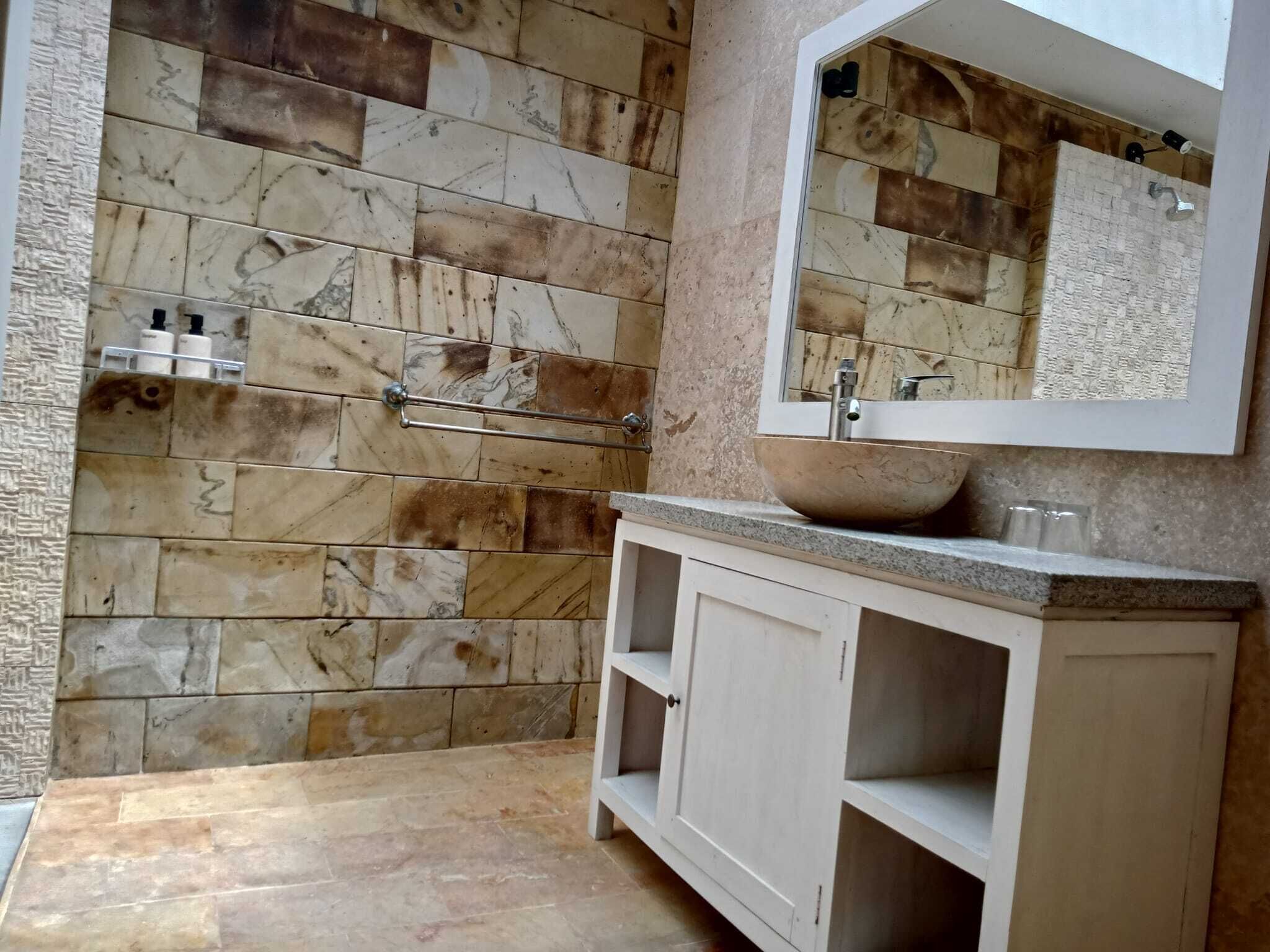 A bathroom with a marble wall, a sink with a bowl, and a mirror.