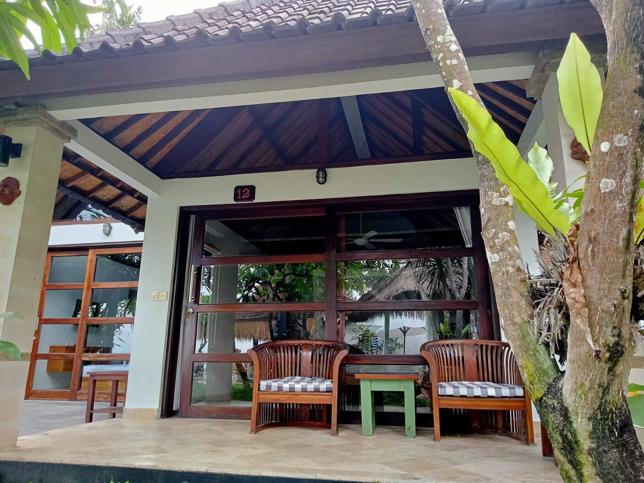 A covered outdoor seating area with two wooden chairs and a small table, a large glass door entrance, and a number '12' sign above the door.