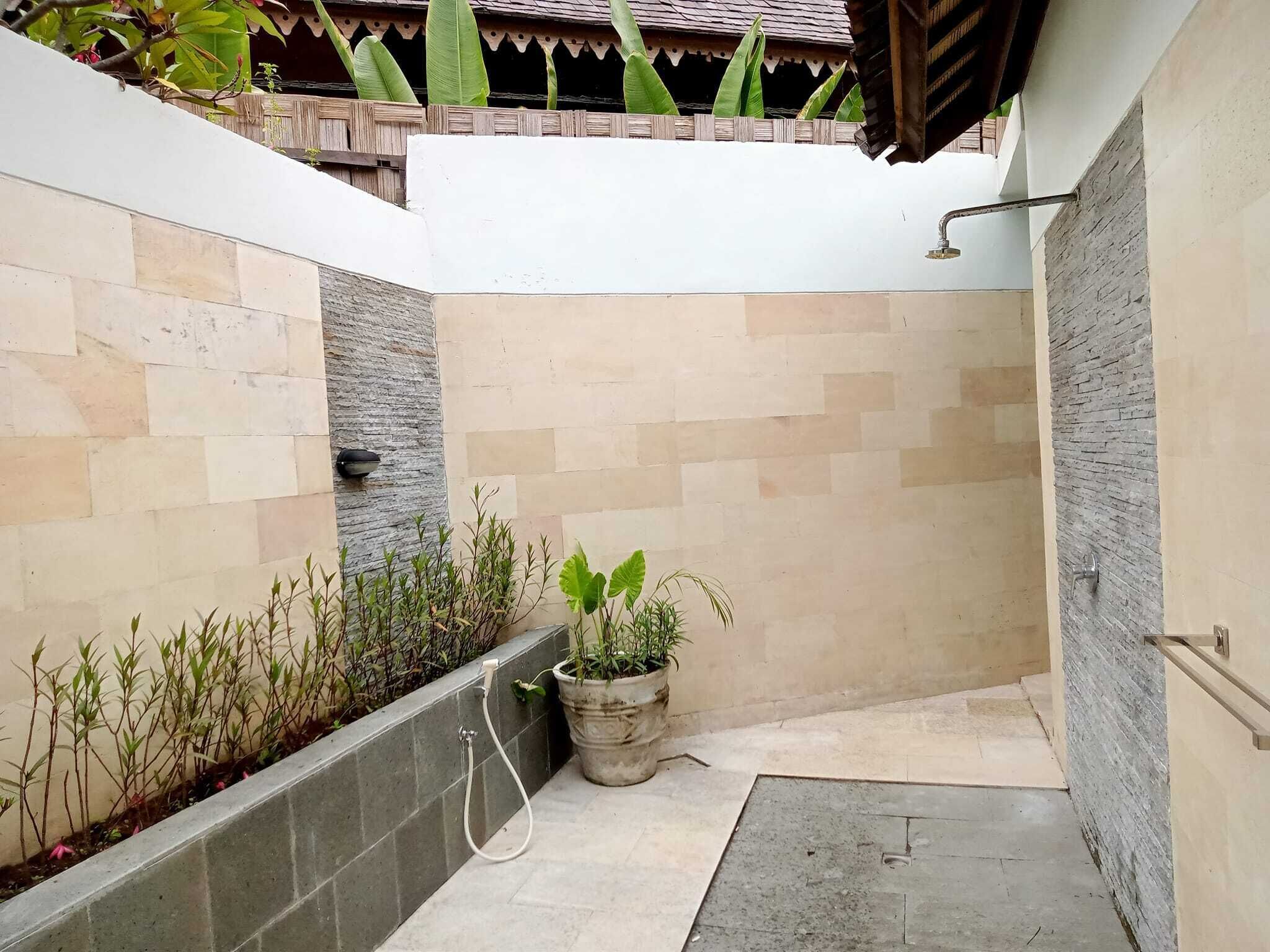 Un pequeño espacio exterior para ducha, con paredes de azulejos, una planta en maceta y un cabezal de ducha.