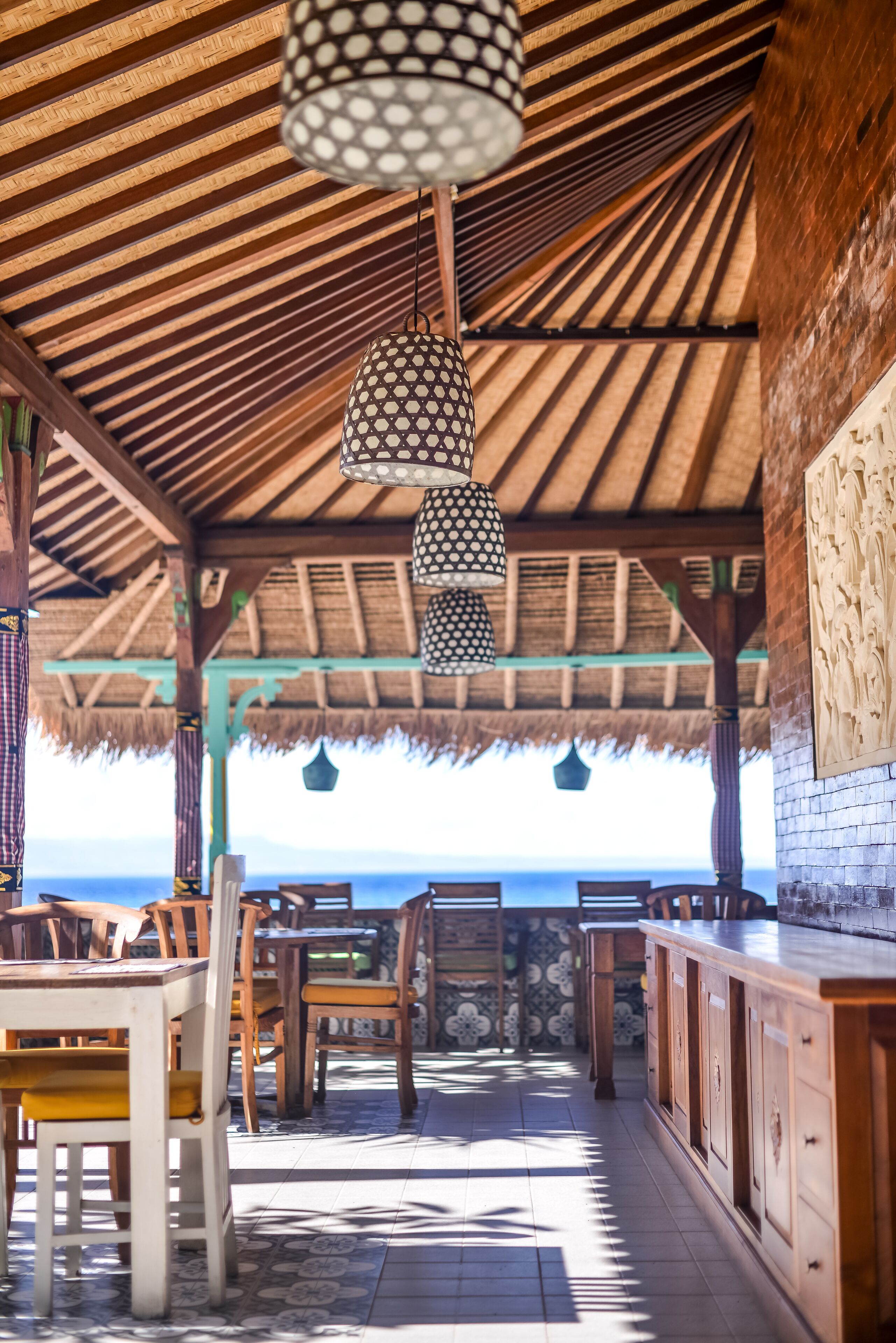 Ein Restaurant direkt am Strand mit Holztischen, hängenden Lampen und Meerblick.