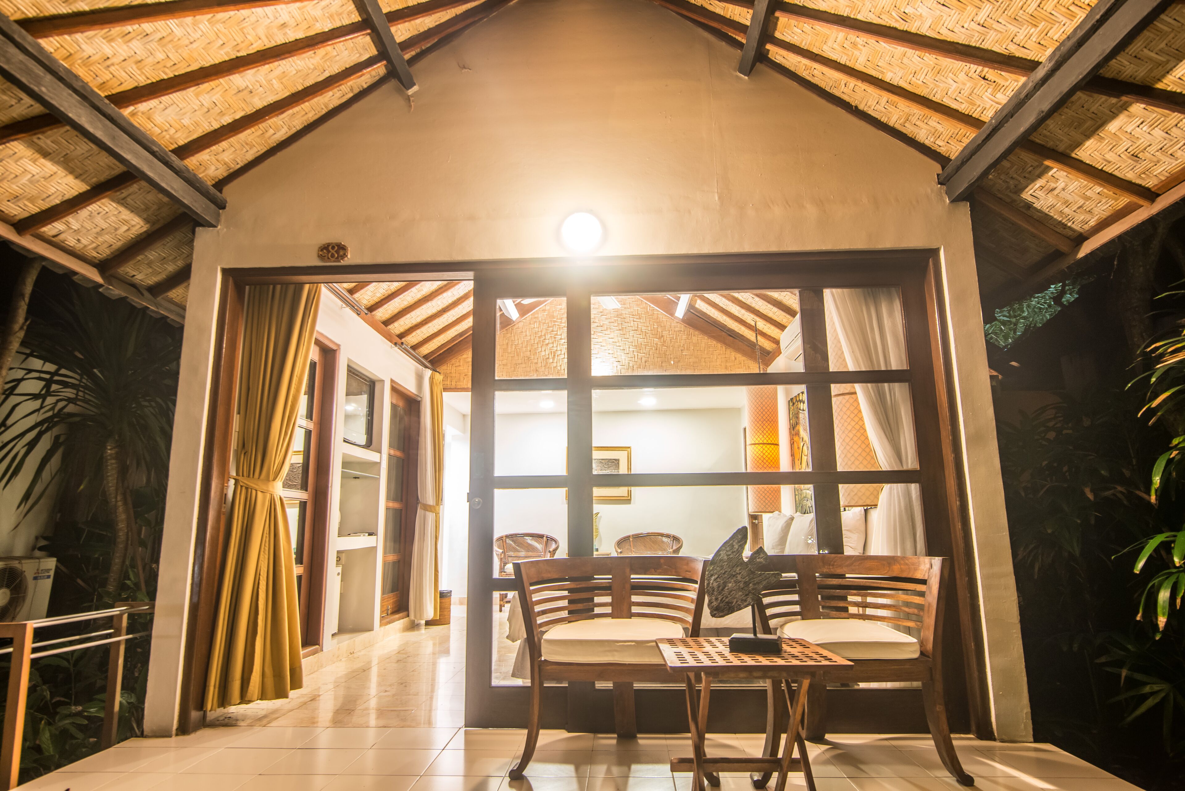 Una habitación con techo de paja, muebles de madera y vistas a través de un ventanal.