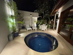 A swimming pool with a white deck and lounge chairs, surrounded by potted plants and a wooden pergola. - Balisanti Bungalows (Manggis)