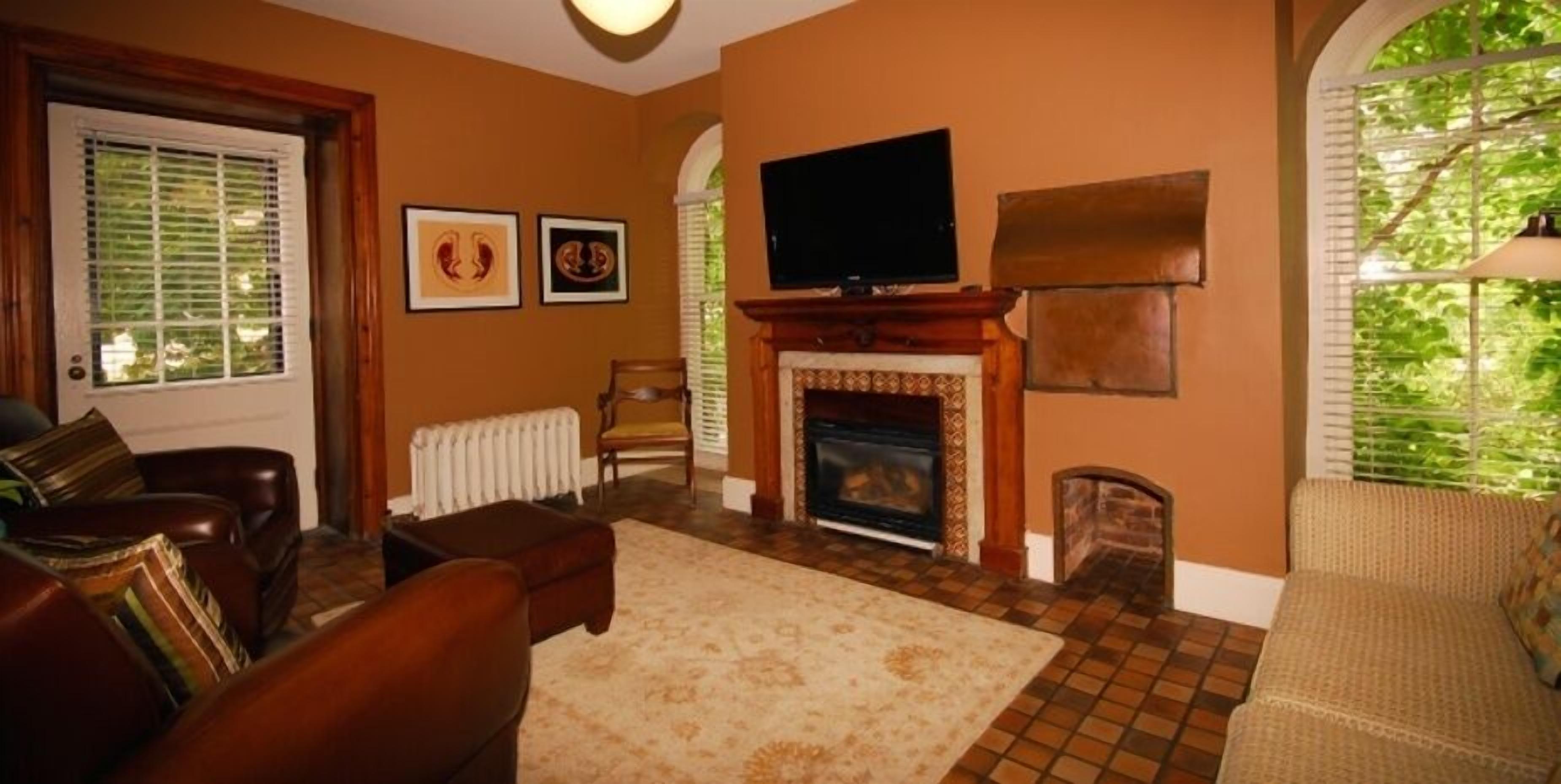 A living room with a fireplace, a television, and a large window with blinds.
