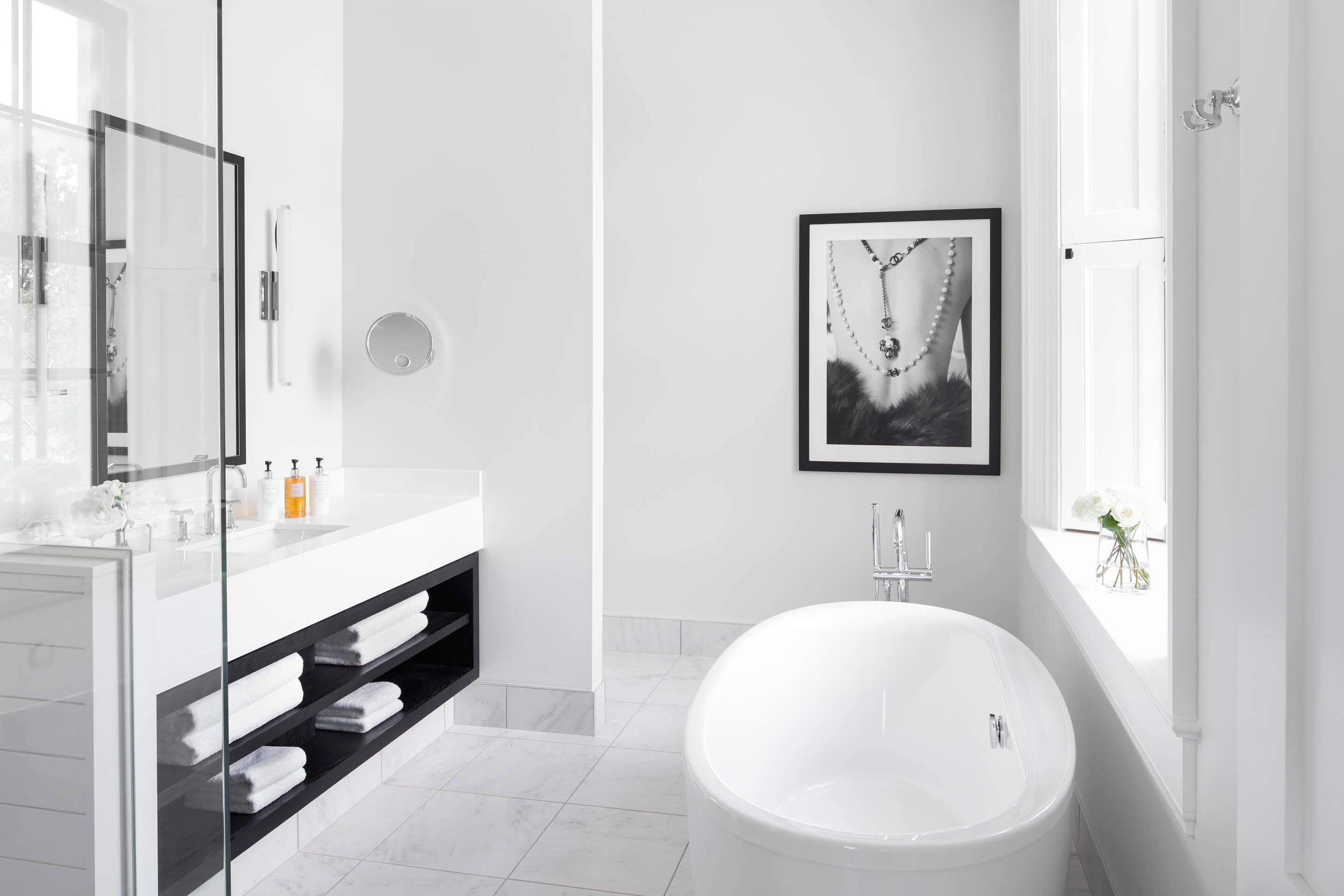 A modern bathroom with a glass shower enclosure, a white bathtub, a large mirror, and a framed picture on the wall.