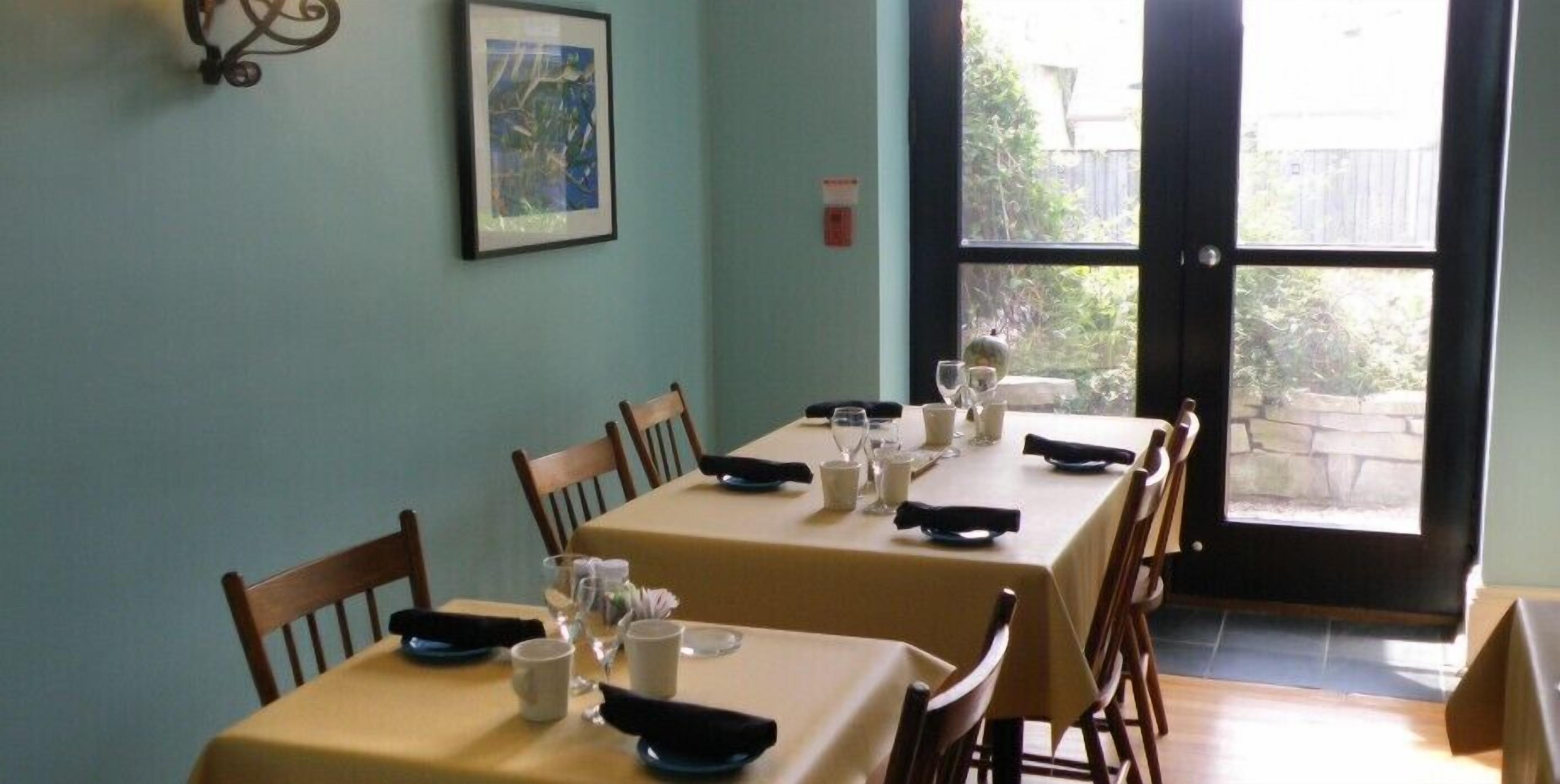 A dining area with two tables, each set with plates, glasses, and napkins. There is a framed picture on the wall and a window with a view of the outside.