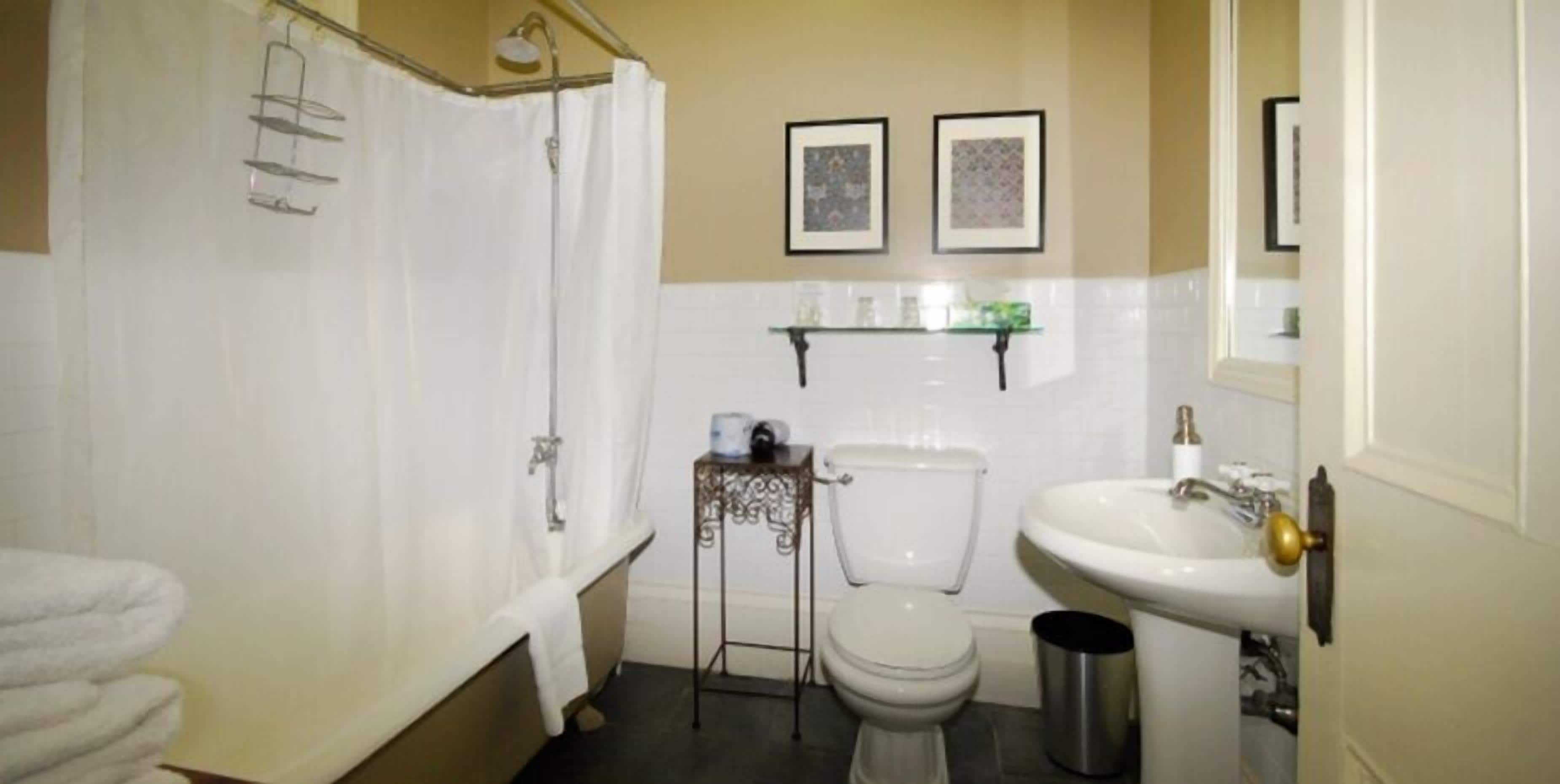 Een badkamer met een bad, toilet, wastafel en een klein tafeltje met toiletartikelen.