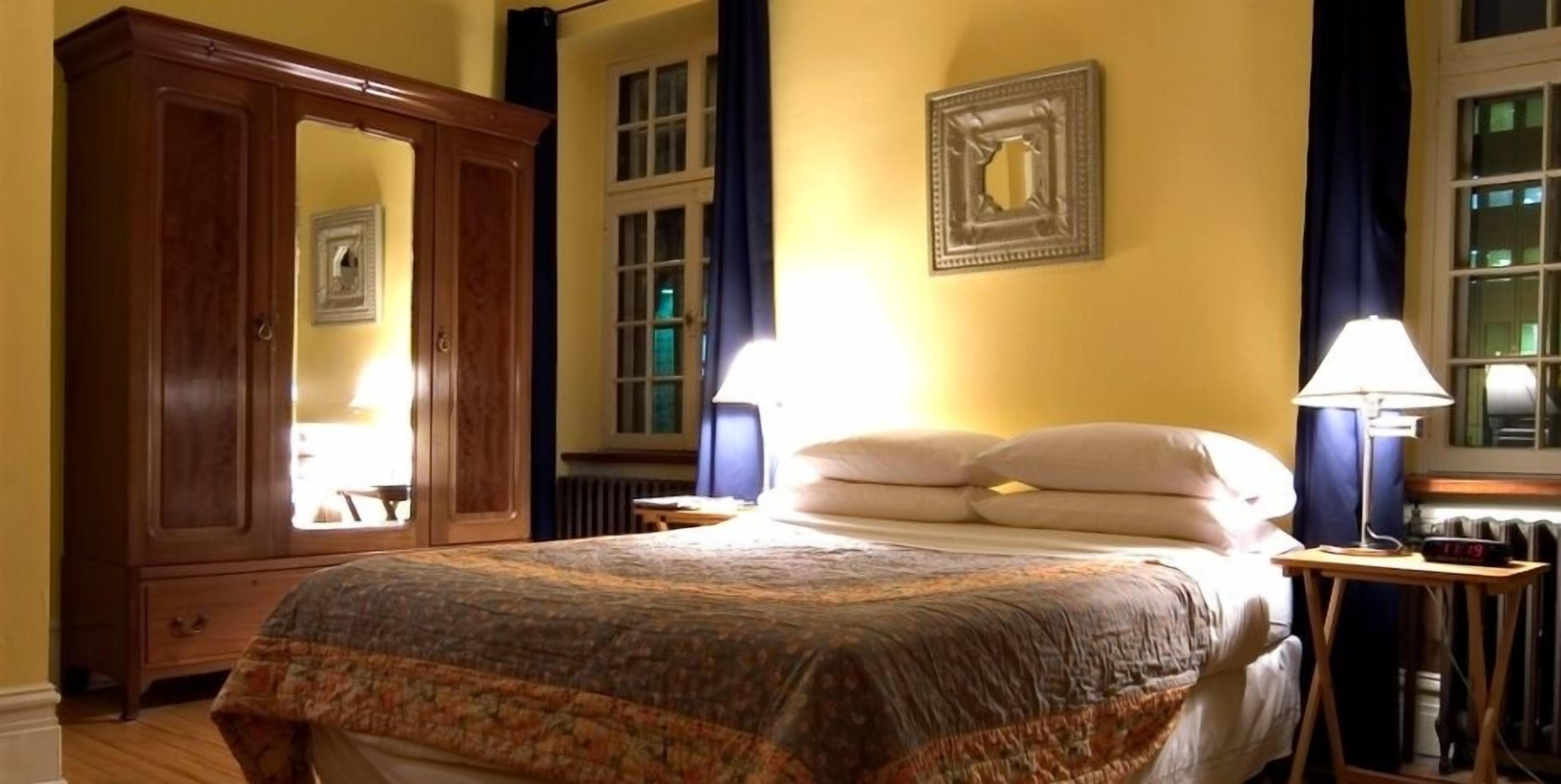 Un dormitorio con una cama grande, un armario de madera, una mesita de noche con lámpara y una ventana con cortinas.