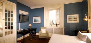 A bedroom with a bed, a desk, a chair, a TV, and a window.