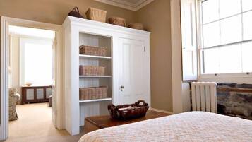 Une chambre à coucher avec un lit, une armoire blanche dotée de paniers en osier, une cheminée en pierre et une vue sur l’extérieur.