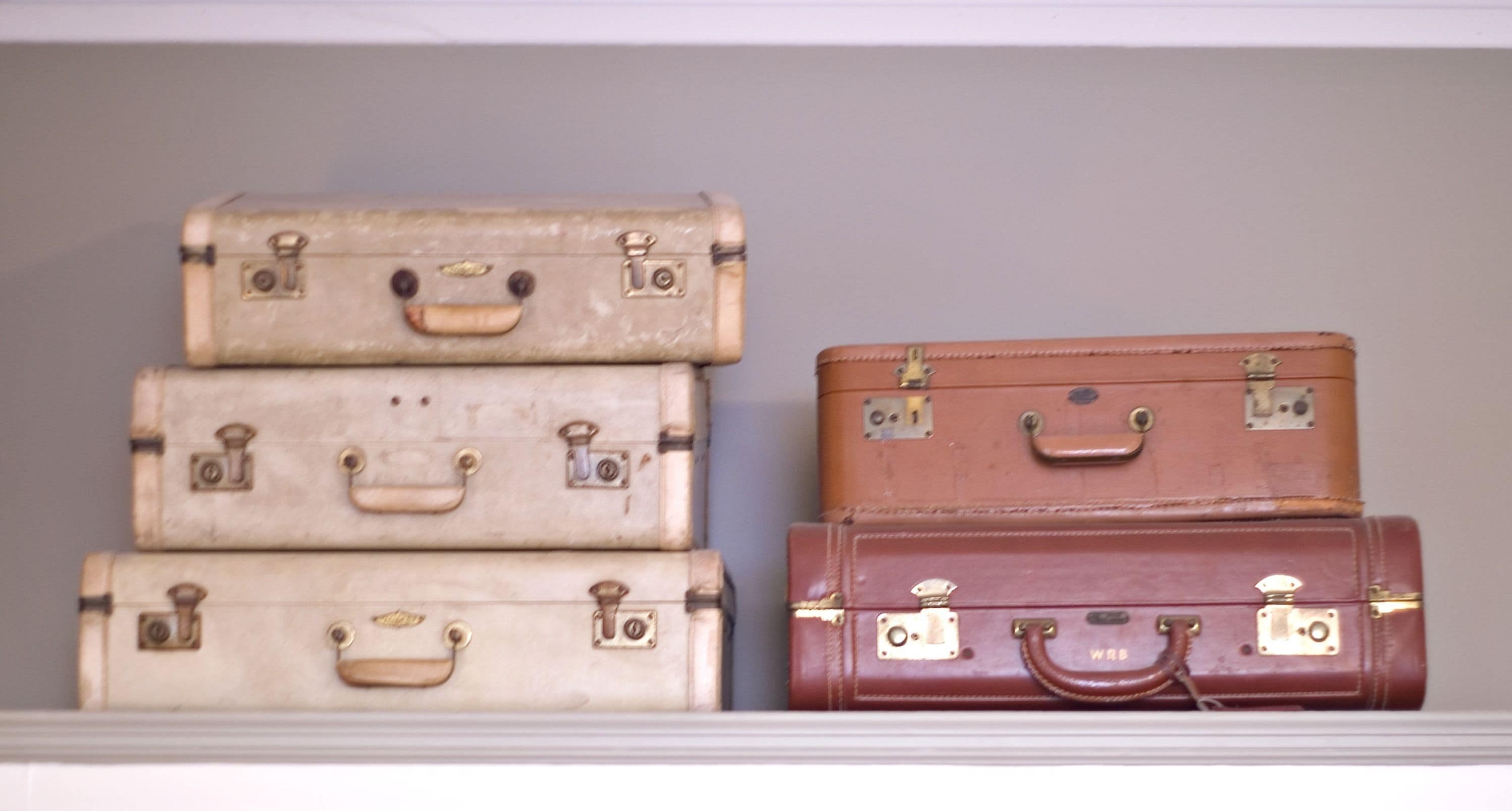 Four vintage suitcases stacked on a shelf.