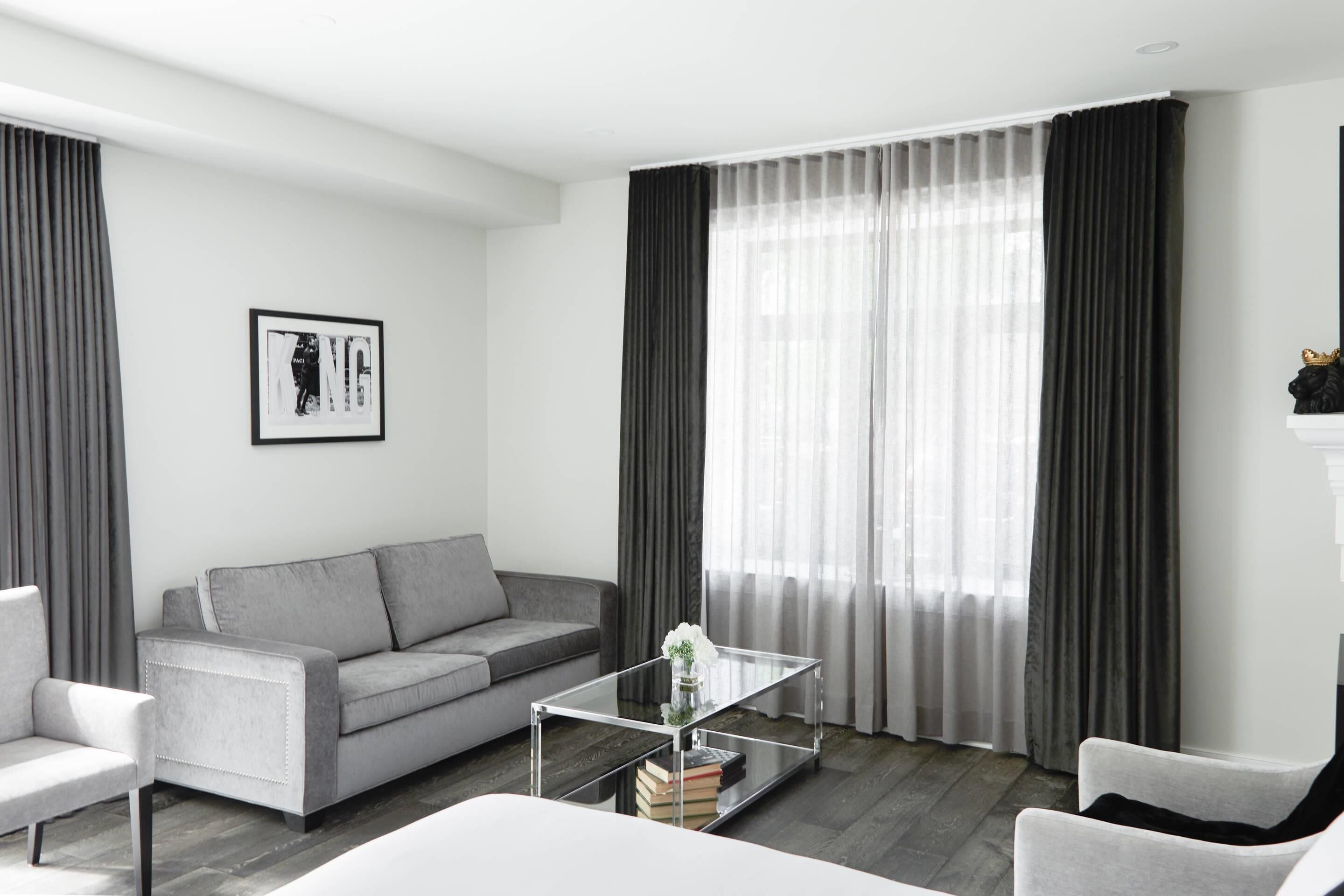 A modern living room with a grey sofa, a glass coffee table with books, and a framed picture on the wall.
