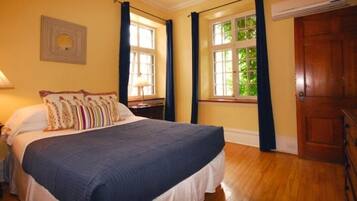 Un lit bien fait, avec une couverture bleue et plusieurs oreillers, une lampe de chevet, une commode en bois et une fenêtre avec des rideaux.