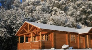 A wooden cabin with a porch, surrounded by snow-covered trees. - BCC Loch Ness Log Cabins (Inverness)