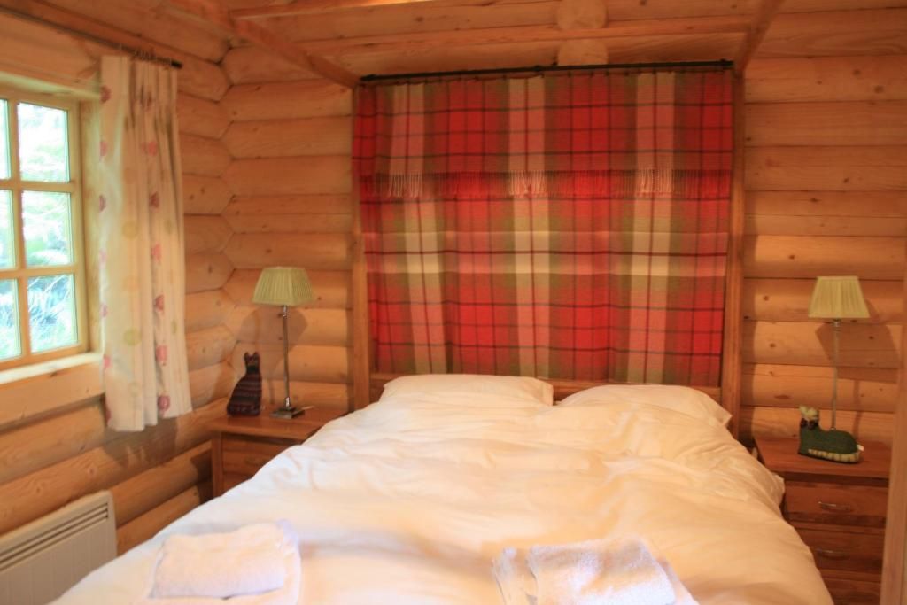 Una camera in una baita di legno, con un letto, due comodini, una finestra con tende e una tenda a quadri.