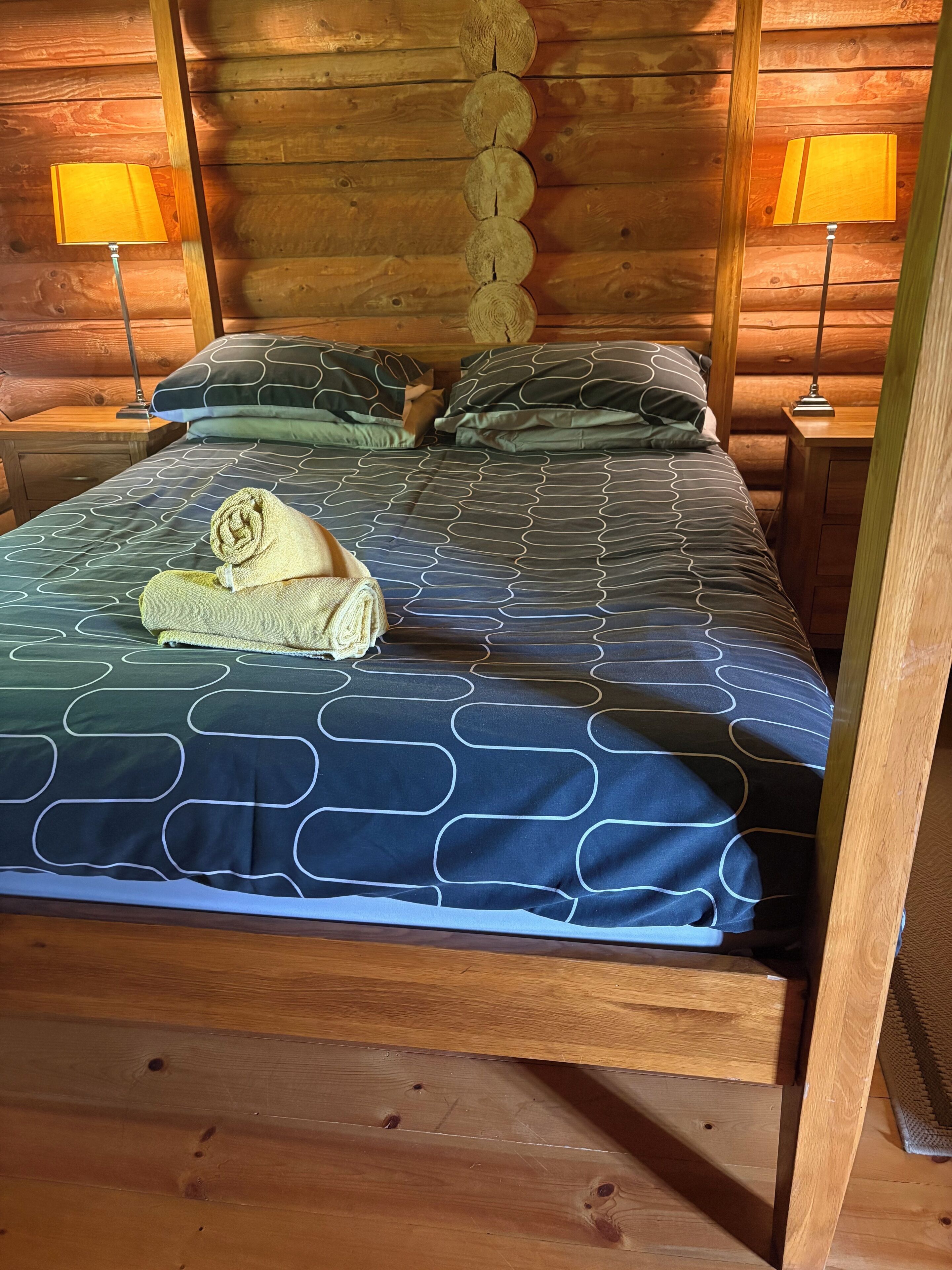 A wooden cabin-style room with a bed, two nightstands, and a wall-mounted lamp.