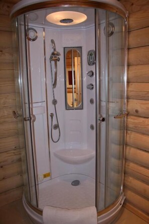 A glass-enclosed shower stall with a sink and control panel, wooden walls, and a mirror. - BCC Loch Ness Log Cabins (Inverness)
