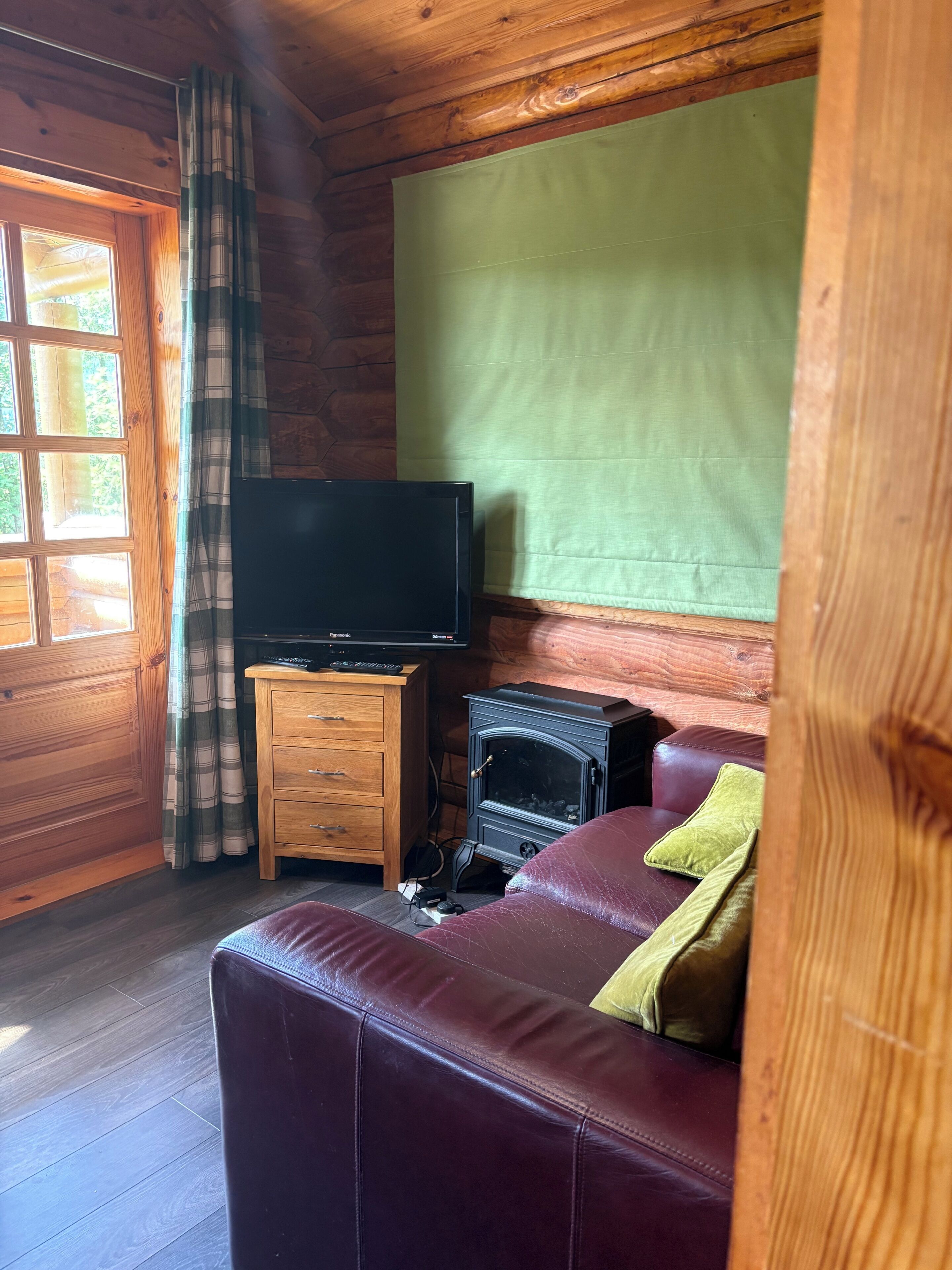 A cozy cabin interior with a television on a wooden stand, a fireplace, and a leather couch.