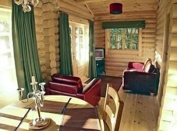 A log cabin interior with a dining area, two sofas, and a television. - BCC Loch Ness Log Cabins (Inverness)