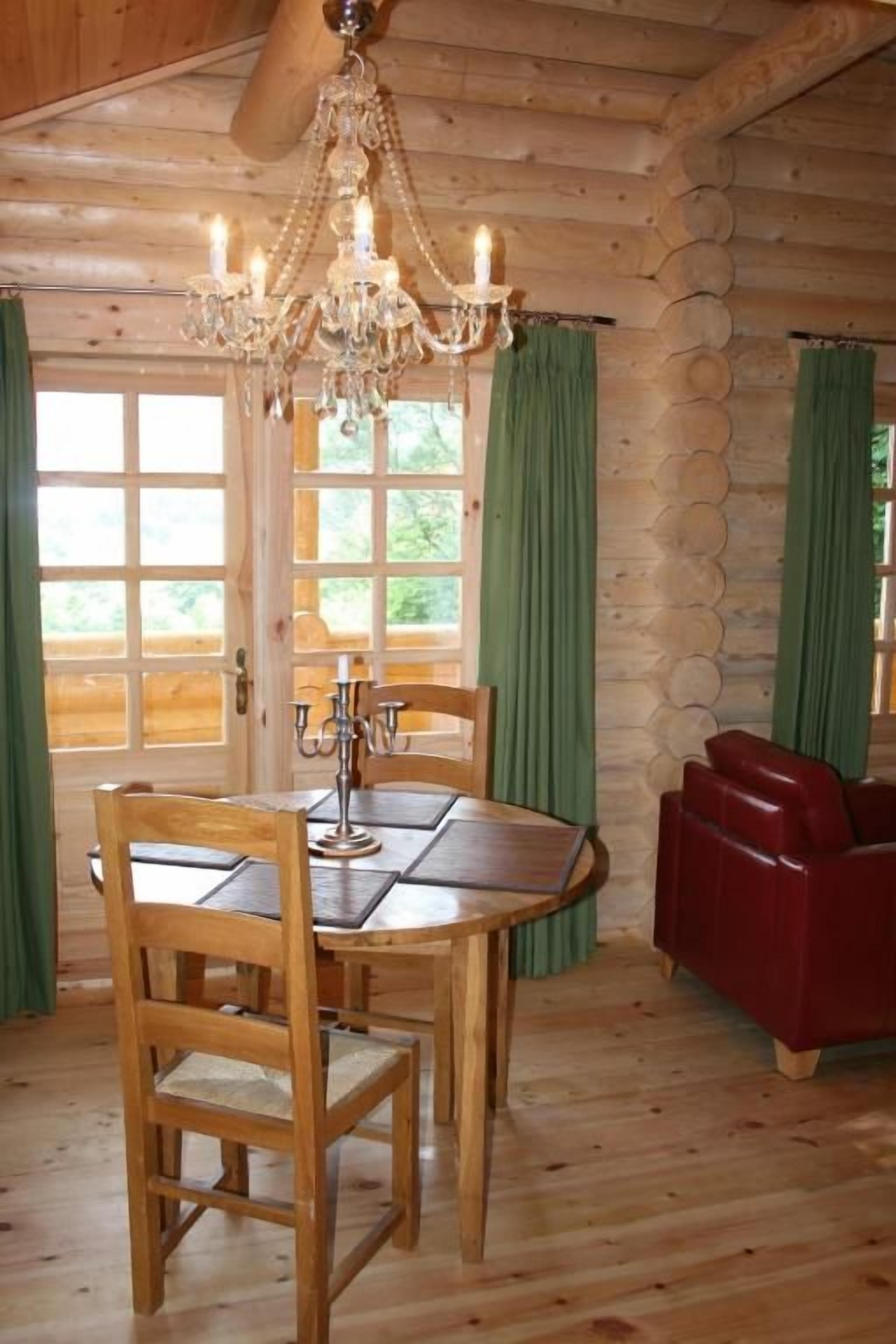 A wooden interior with a dining table, chairs, a chandelier, and a red sofa.