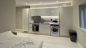 A modern hotel room with a large bed, a small kitchenette, a washing machine, and a trash bin. - Buckingham Apartments (High Wycombe)