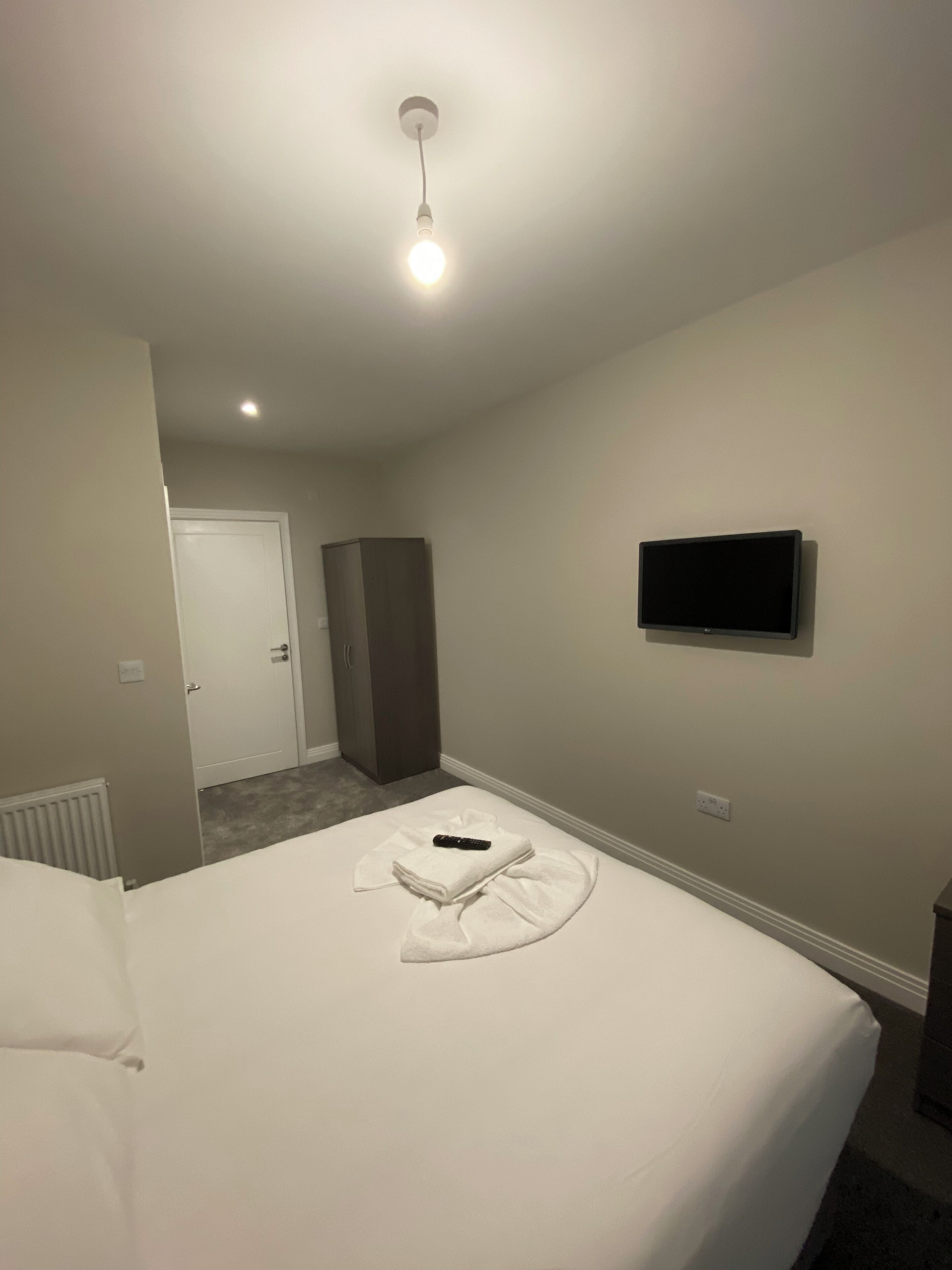 A hotel room with a bed, a TV on the wall, a door, and a wardrobe.