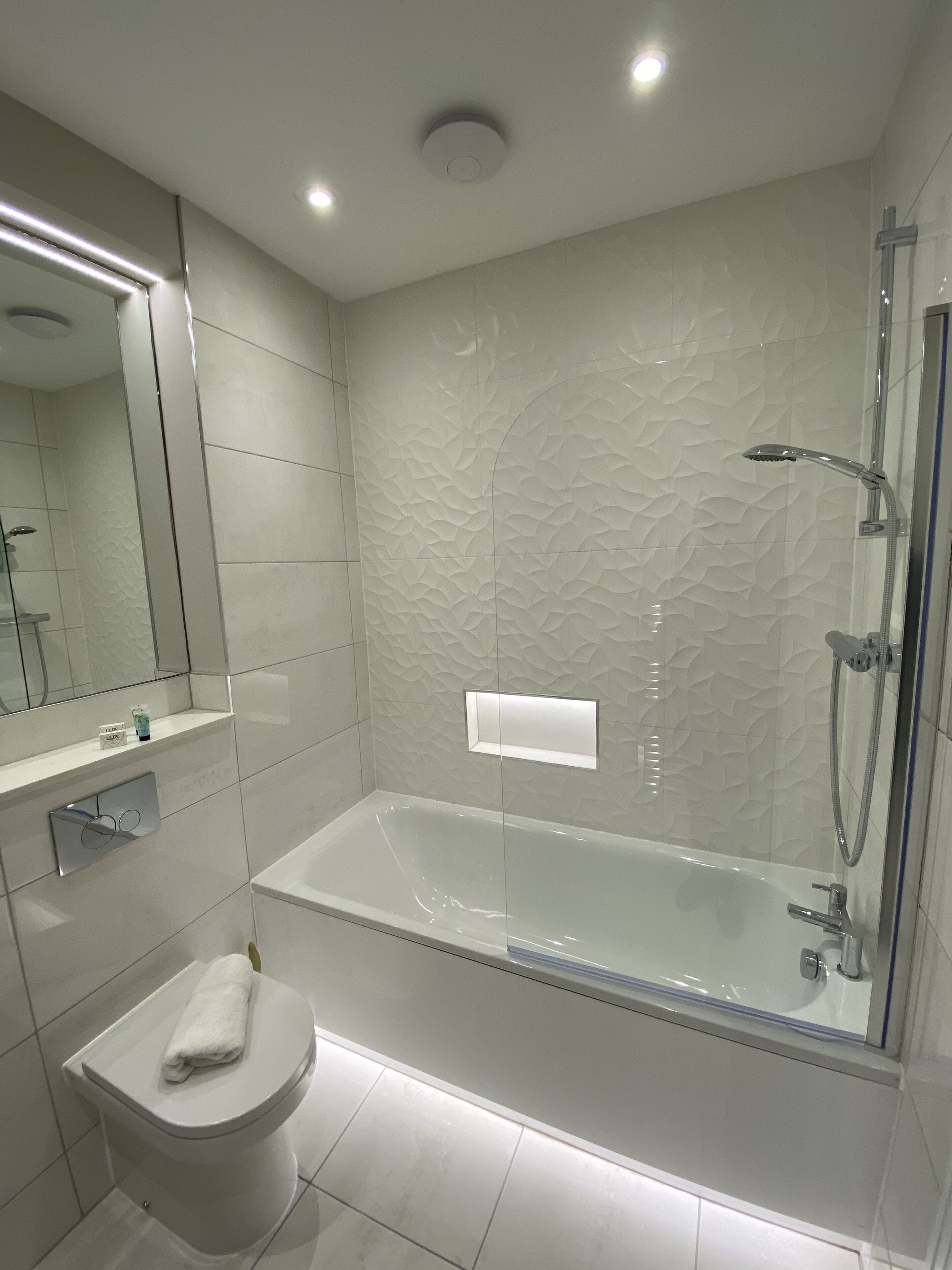 Un baño moderno con ducha envuelta en vidrio, inodoro blanco y tocador con espejo.