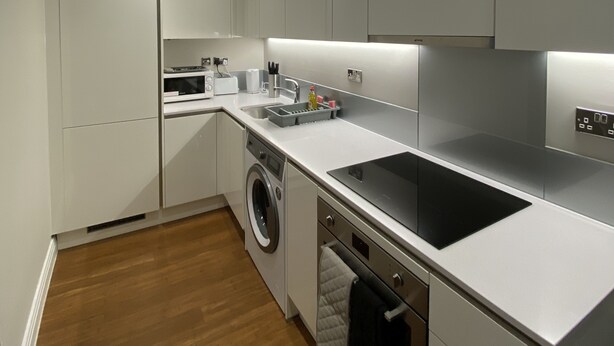 A modern kitchen with white cabinets, a stainless steel sink, and a built-in oven. - Buckingham Apartments (High Wycombe)