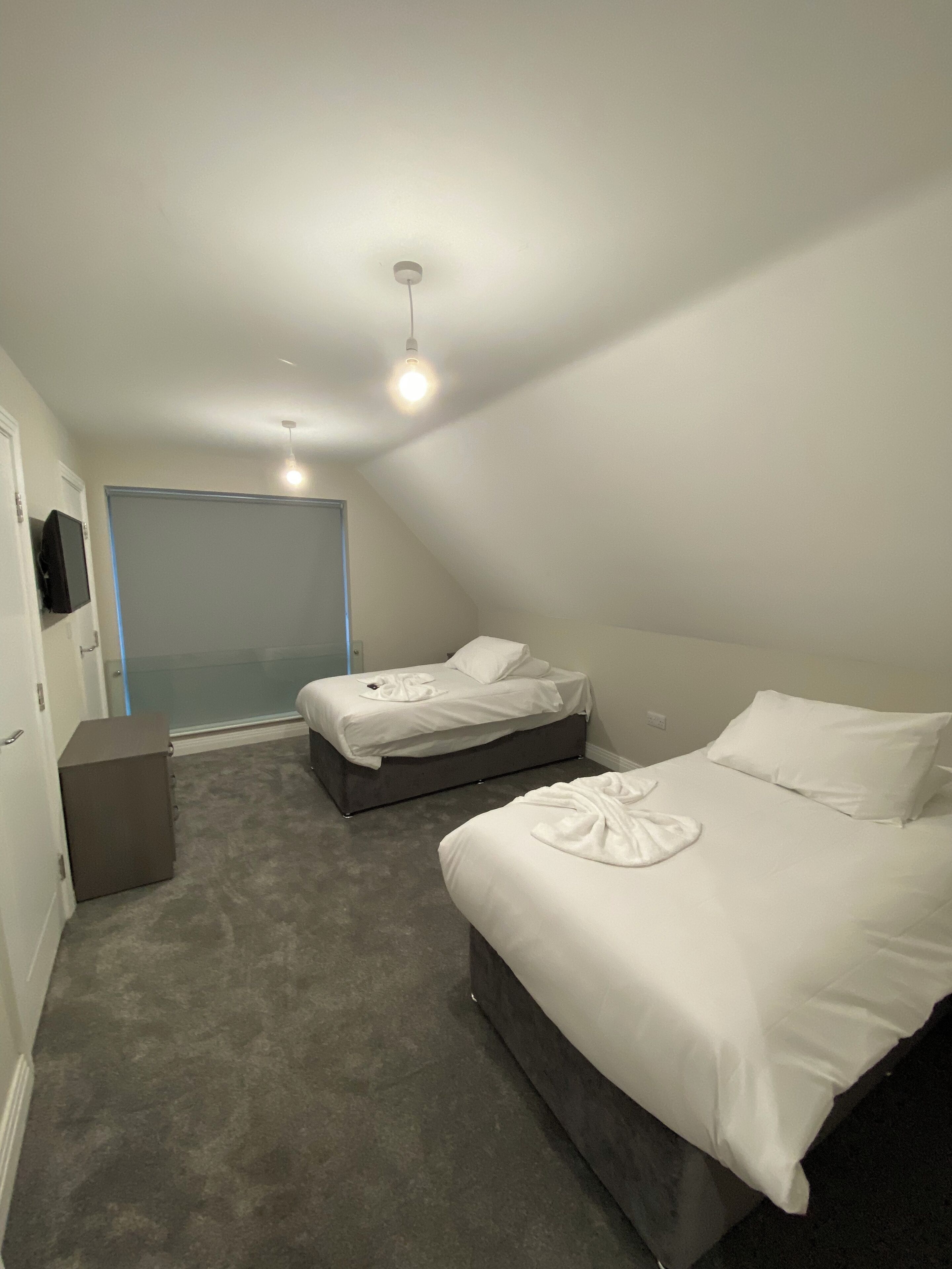A bedroom with two beds, a small desk, and a television on the wall.