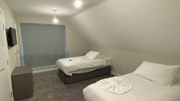 A bedroom with two beds, a small desk, and a television on the wall.