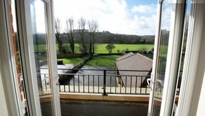 A view from a balcony with a railing, overlooking a green landscape with trees and a building in the distance. - Buckingham Apartments (High Wycombe)